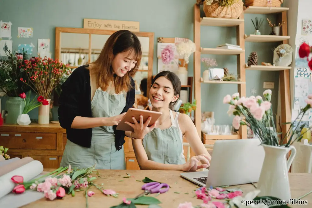 Fröhliche Menschen an einem mit Blumenblüten übersäten Tisch, in ein Tablet blickend