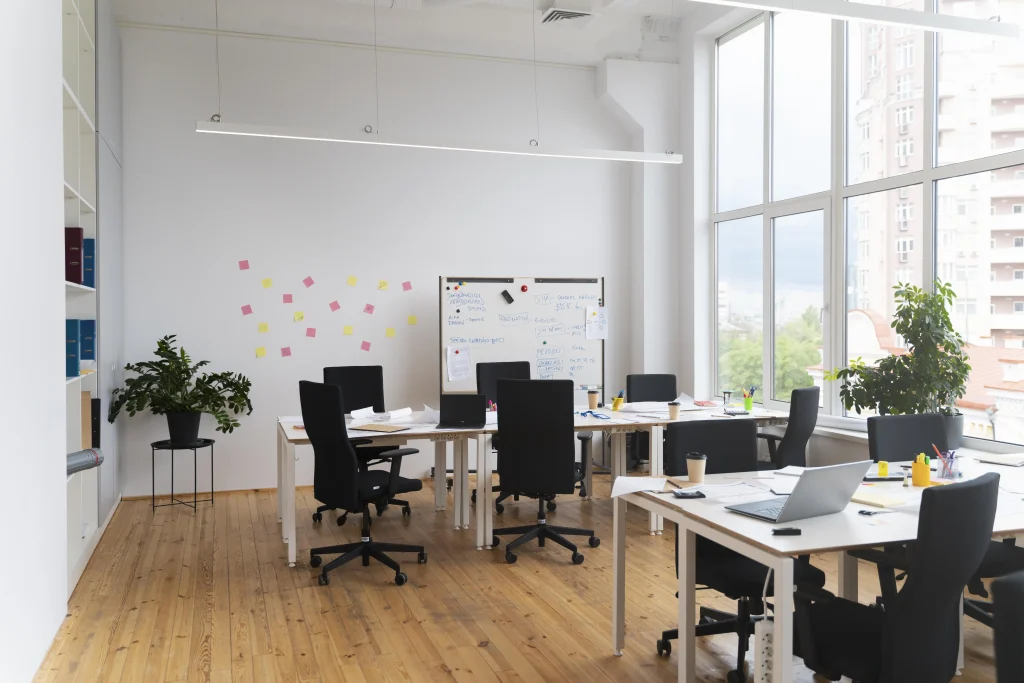 Auf dem Bild ist ein leerer Coworking Space zu sehen. In diesem befinden sich mehrere Tische und Stühle, wie auch eine kleinere Tafel.