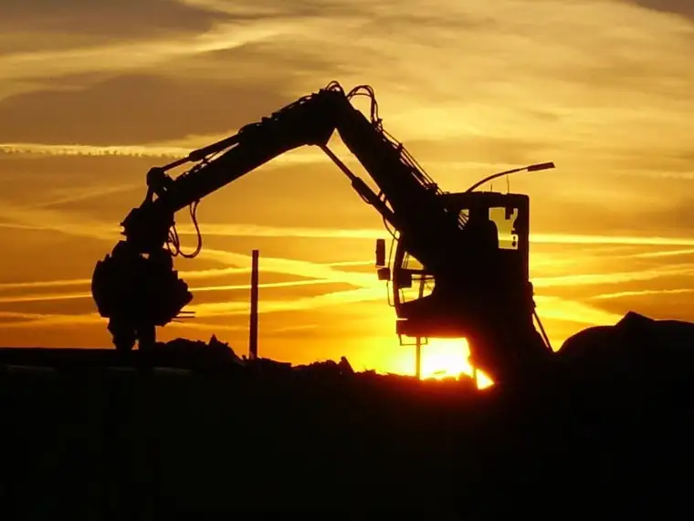 Die Silhouette eines Baggers auf einer Mülldeponie im Sonnenuntergang