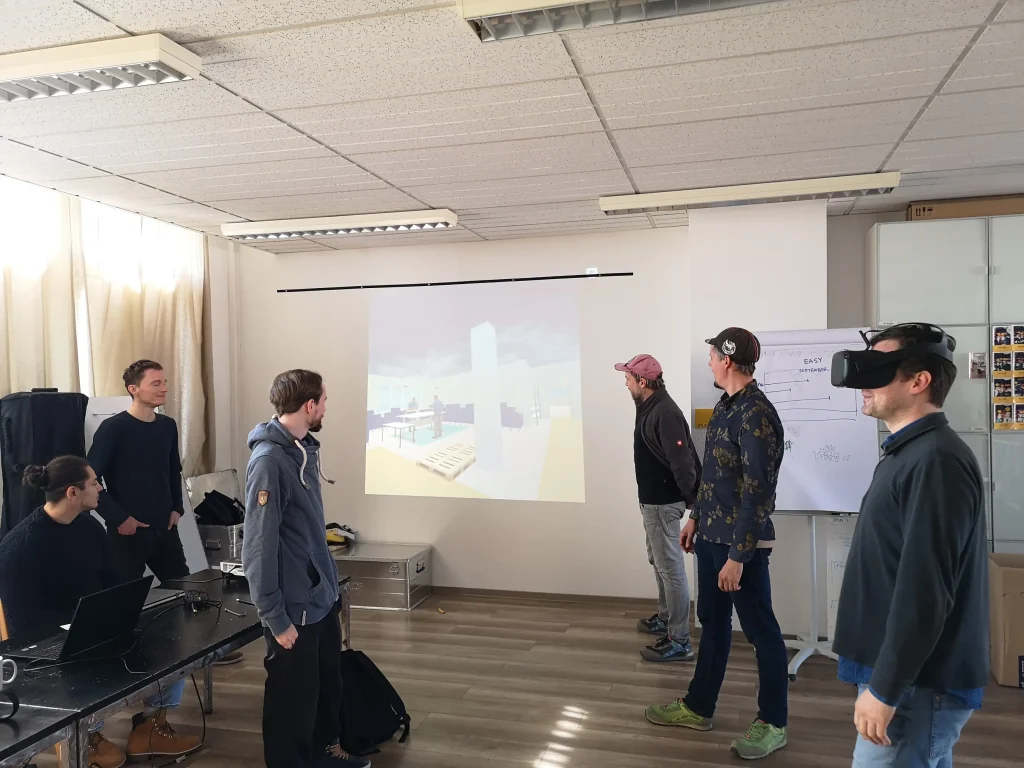 Auf dem Bild sind sechs Personen zu sehen, eine Person hat eine VR-Brille auf und kann die neu angeordneten Arbeitsbereiche in der Fertigung sehen.