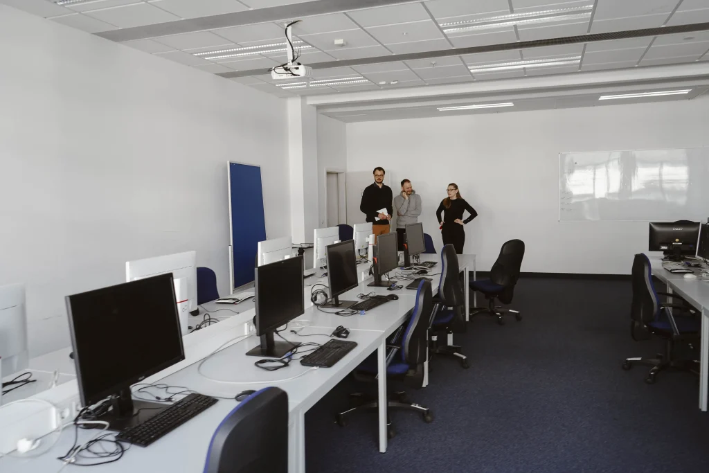 2 Mitarbeitende und Projektmitarbeiter schauen sich die Computerarbeitsplätze von BBQ an
