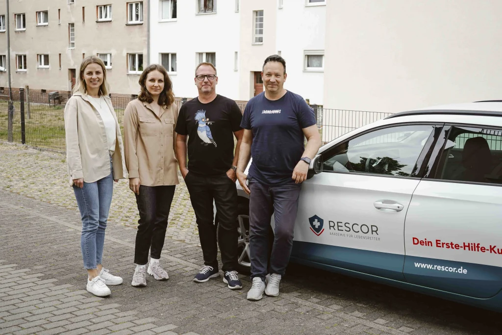 Vier Personen stehen vor einem Firmenauto