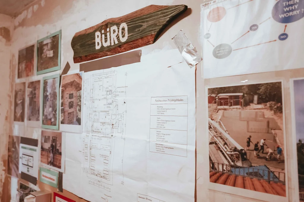 Eine Pinnwand mit Fotos und einem Schild, welches zum Büro führt