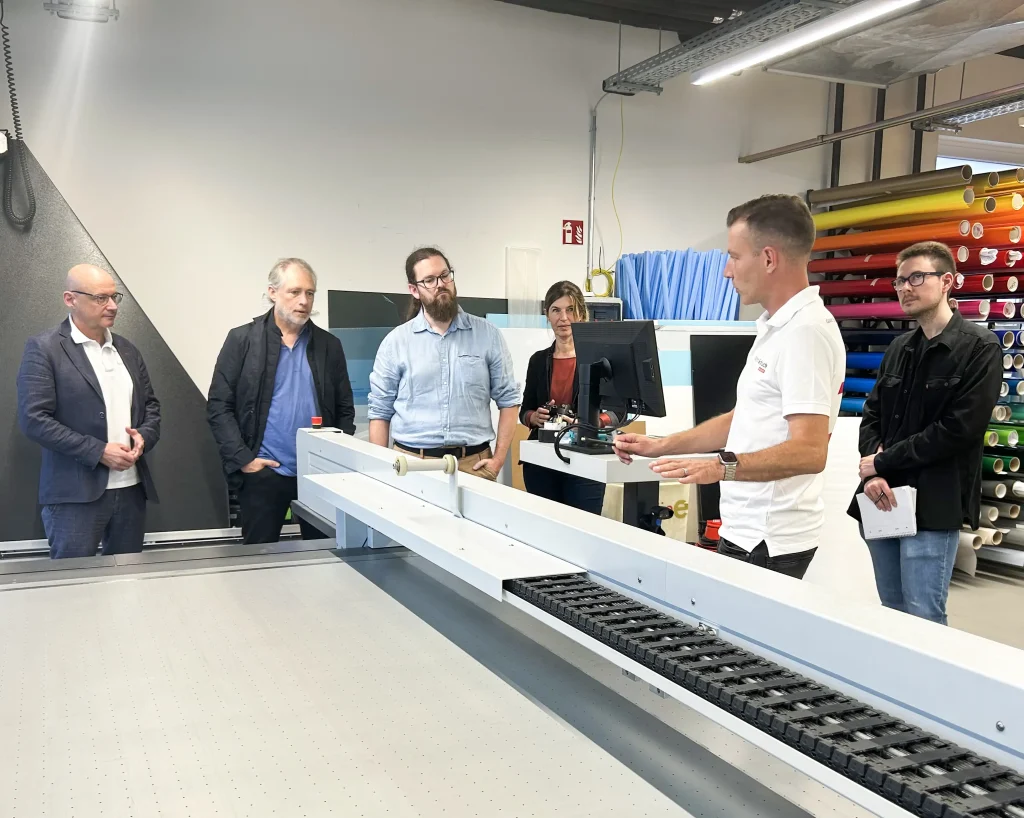 Klima-Coaches betrachten eine Maschine in der Produktion der Firma Optiplan