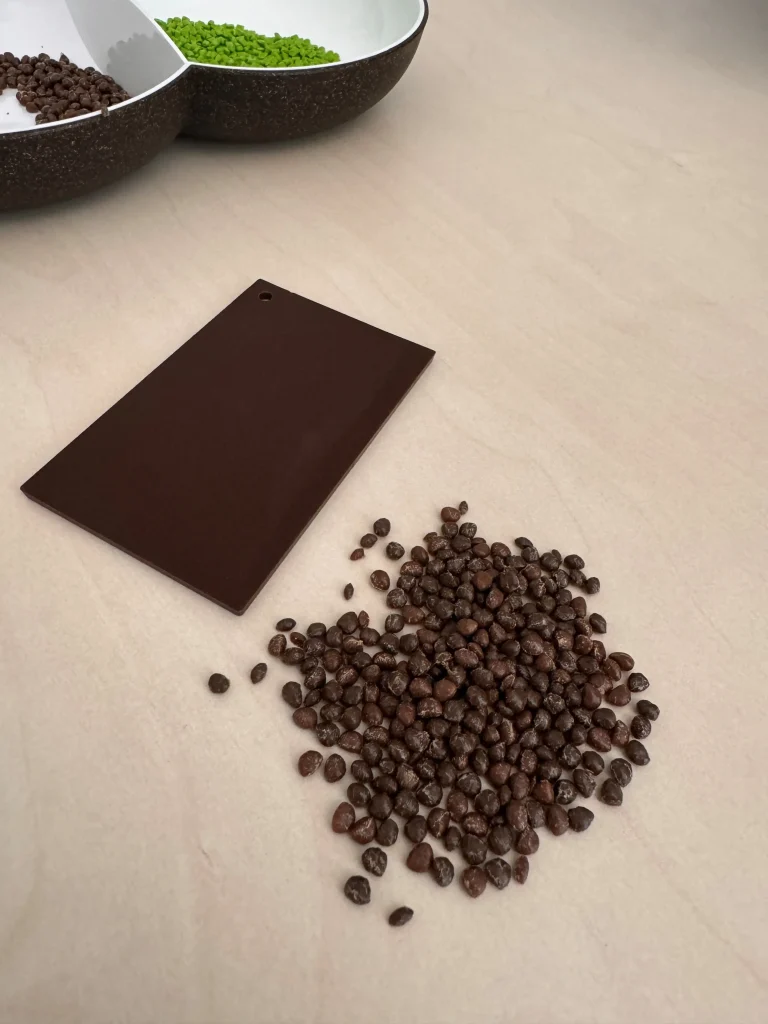 Braunes Granulat und eine Schüssel mit braunem und grünem Granulat, sowie eine braune Musterplatte aus Biokunststoffen auf der Basis von nachwachsenden Rohstoffen