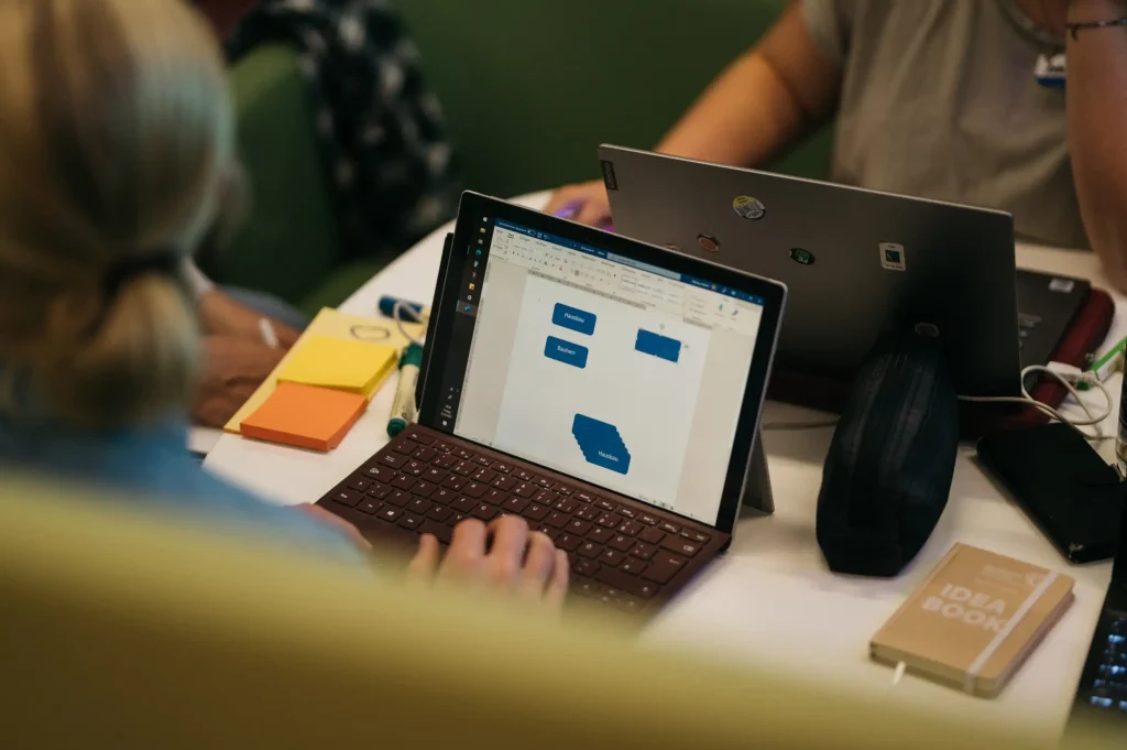 Mehrere Personen arbeiten gemeinsam an einem Tisch mit Laptops, Notizzetteln und einem geöffneten Diagramm-Dokument.