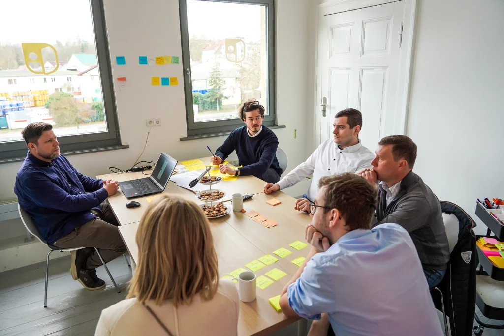 Eine Gruppe sitzt am Tisch, viele Post-Its, eine Person am Laptop, die eine Software testet