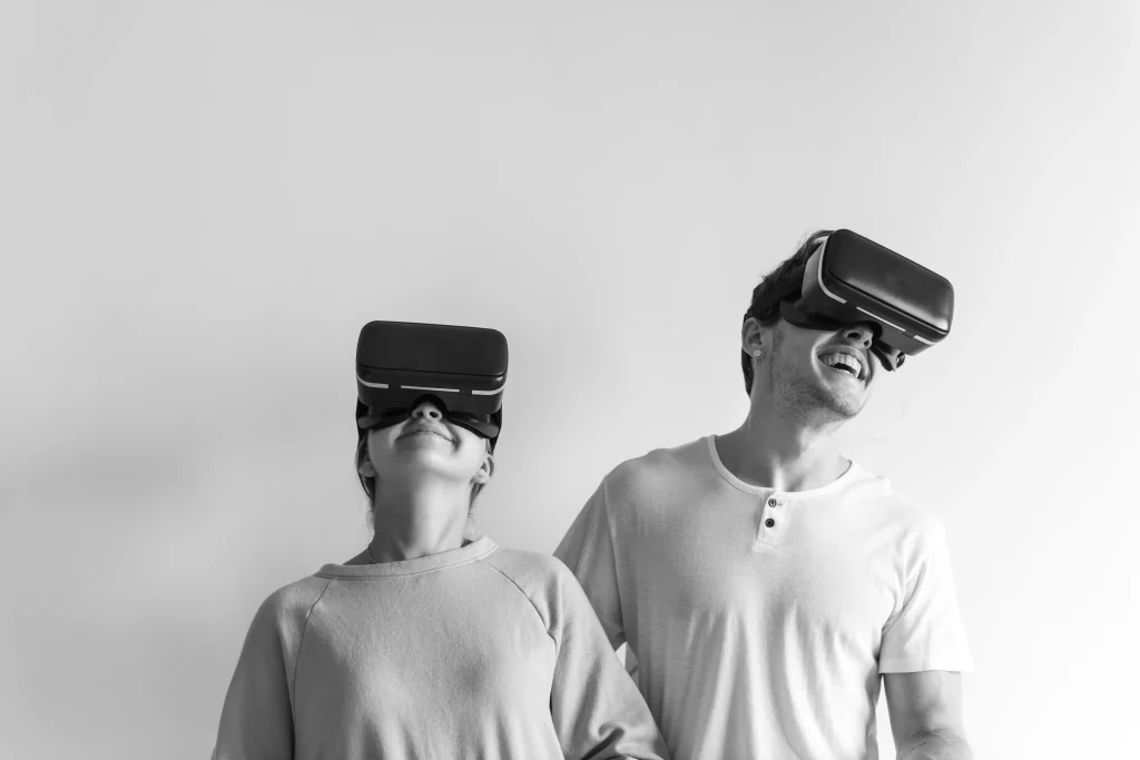 Es sind zwei Personen mit VR-Brille zu sehen, die nebeneinander stehen und lachen.