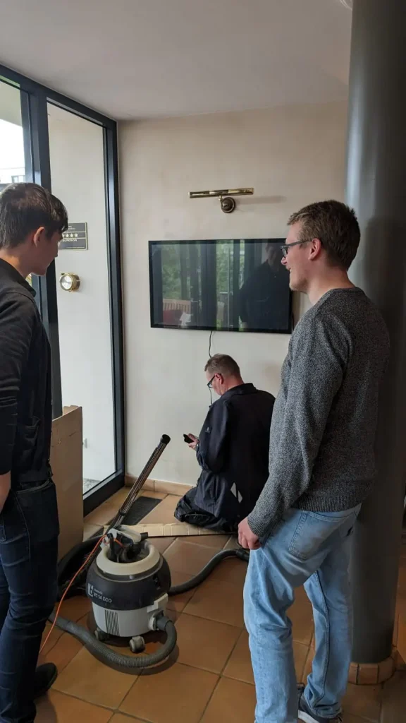 Drei Männer installieren einen Monitor an einer Wand.